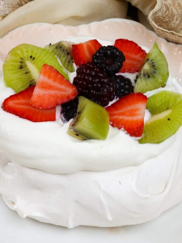 a pavlova on a white plate topped with whipped cream, blackberries, strawberries, and kiwi fruit
