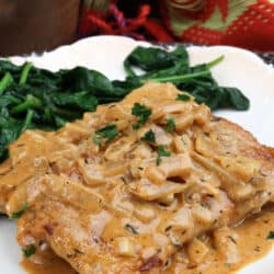 one pork chop smothered with an onion gravy on a white plate next to sauteed spinach