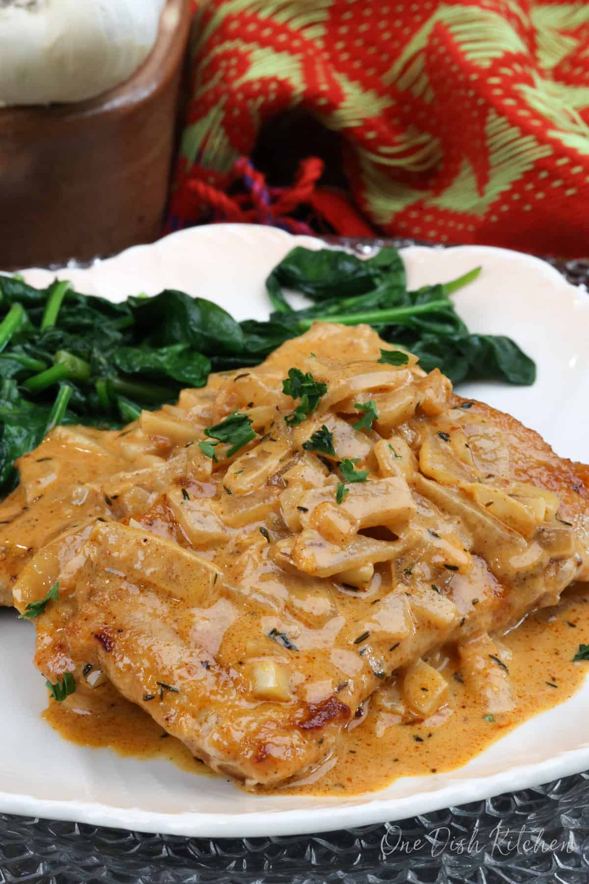 one pork chop smothered with an onion gravy on a white plate next to sauteed spinach