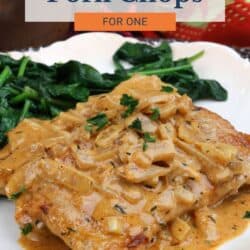 smothered pork chops on a white plate next to cooked spinach.