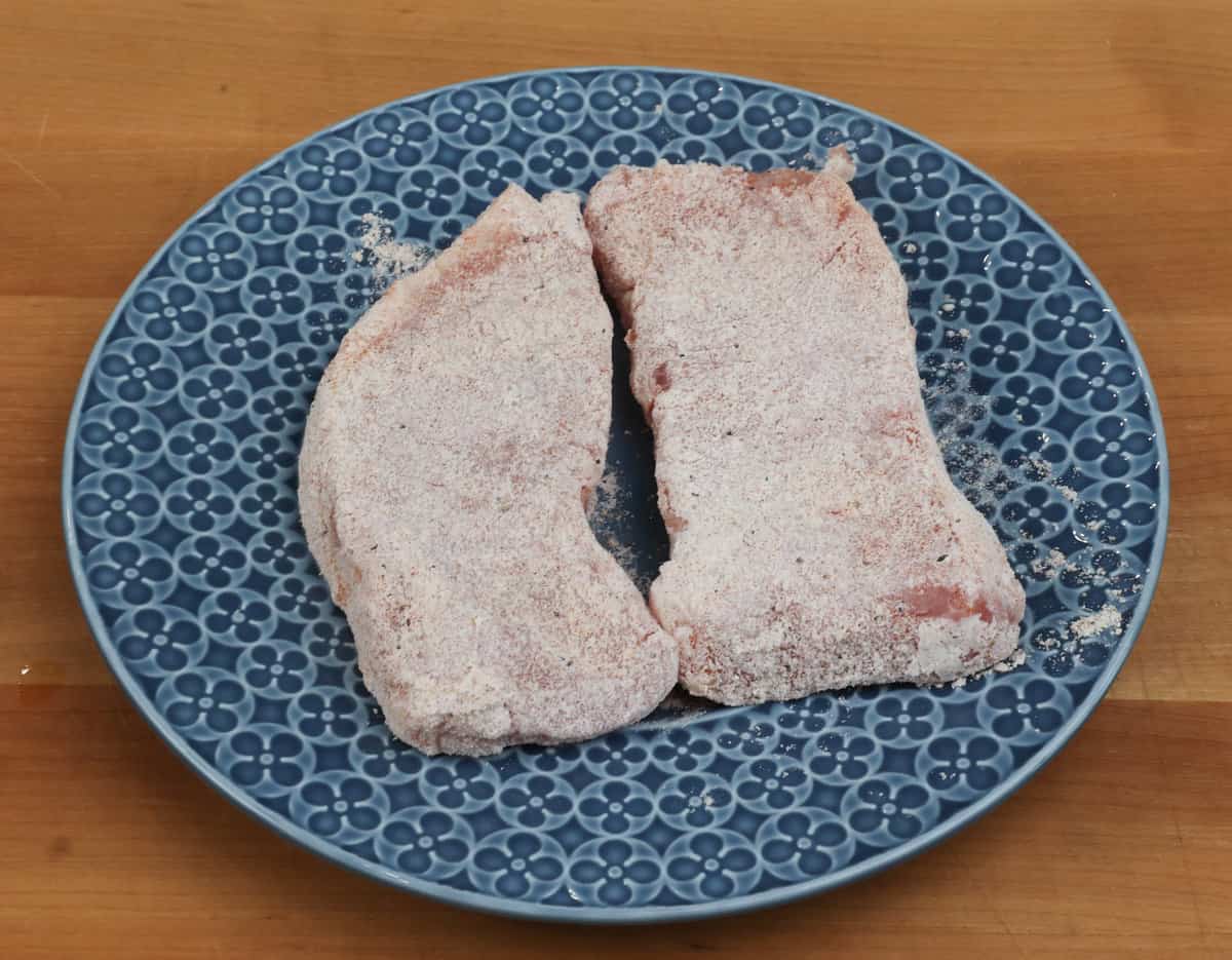 two pork chops covered in flour on a blue plate.
