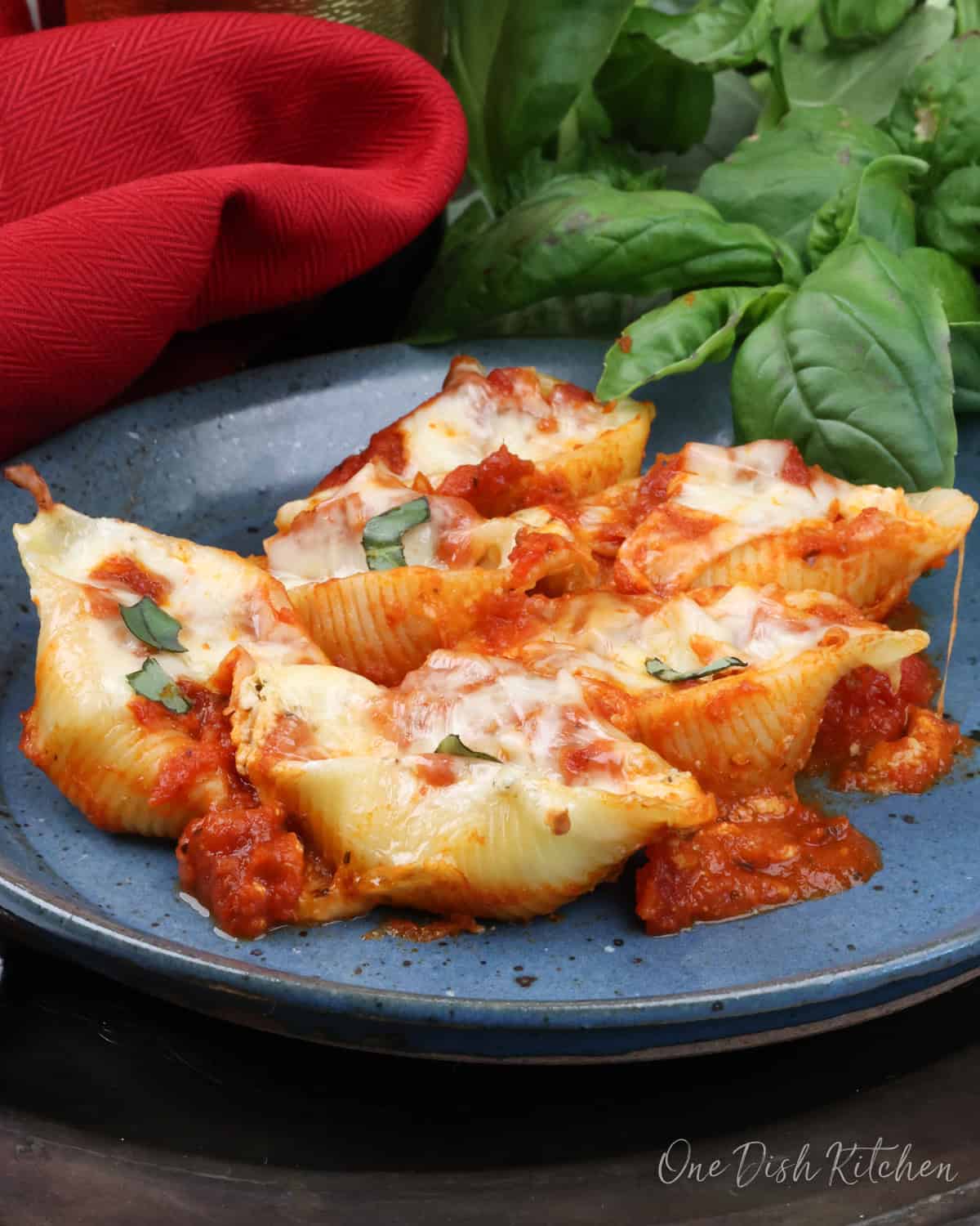 six jumbo pasta shells stuffed with ricotta and mozzarella cheese on a blue plate next to a red napkin.