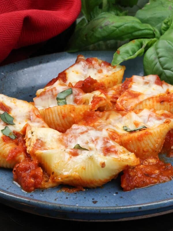 six jumbo pasta shells stuffed with ricotta and mozzarella cheese on a blue plate next to a red napkin.