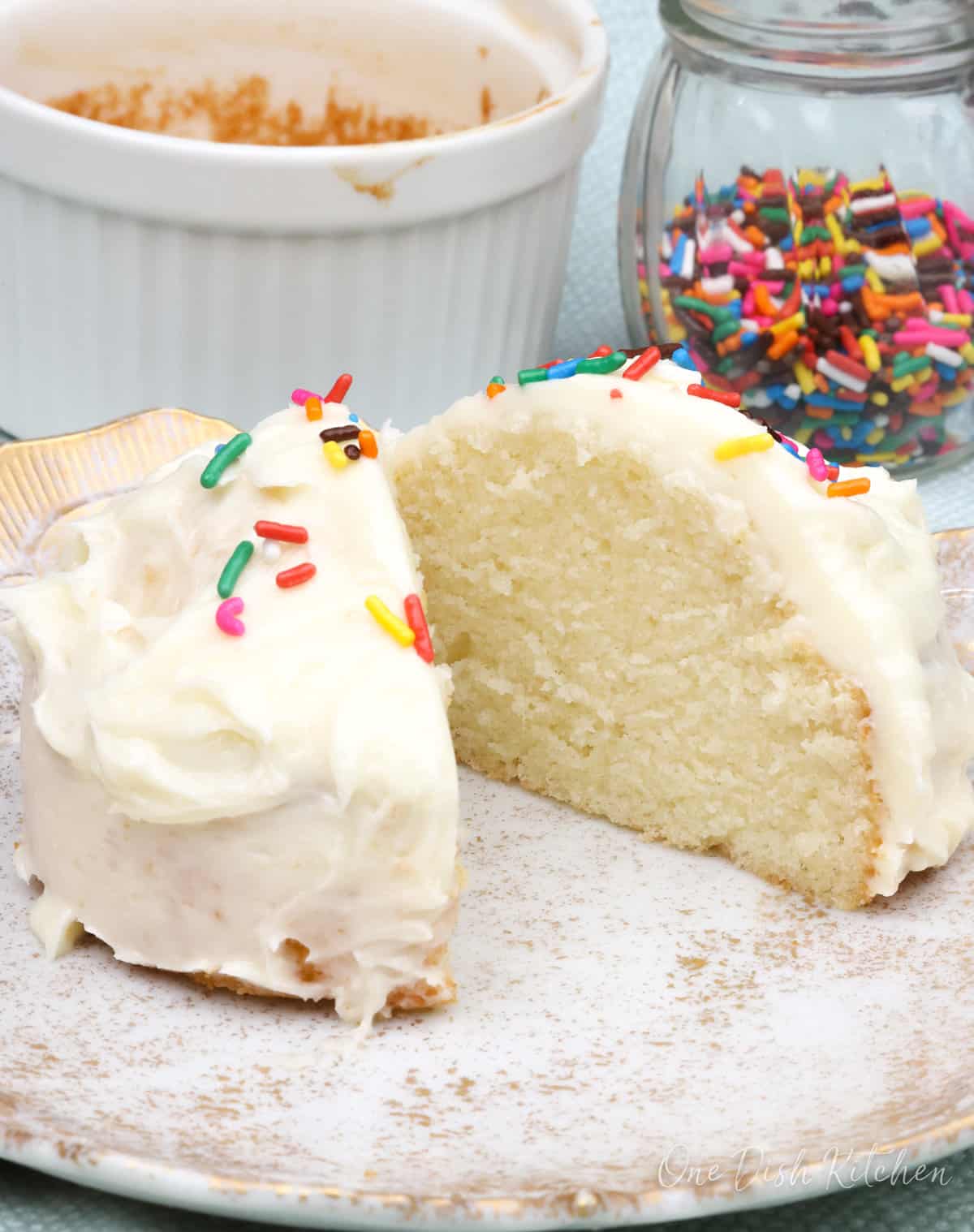 a slice of white cake on a plate next to a jar of sprinkles