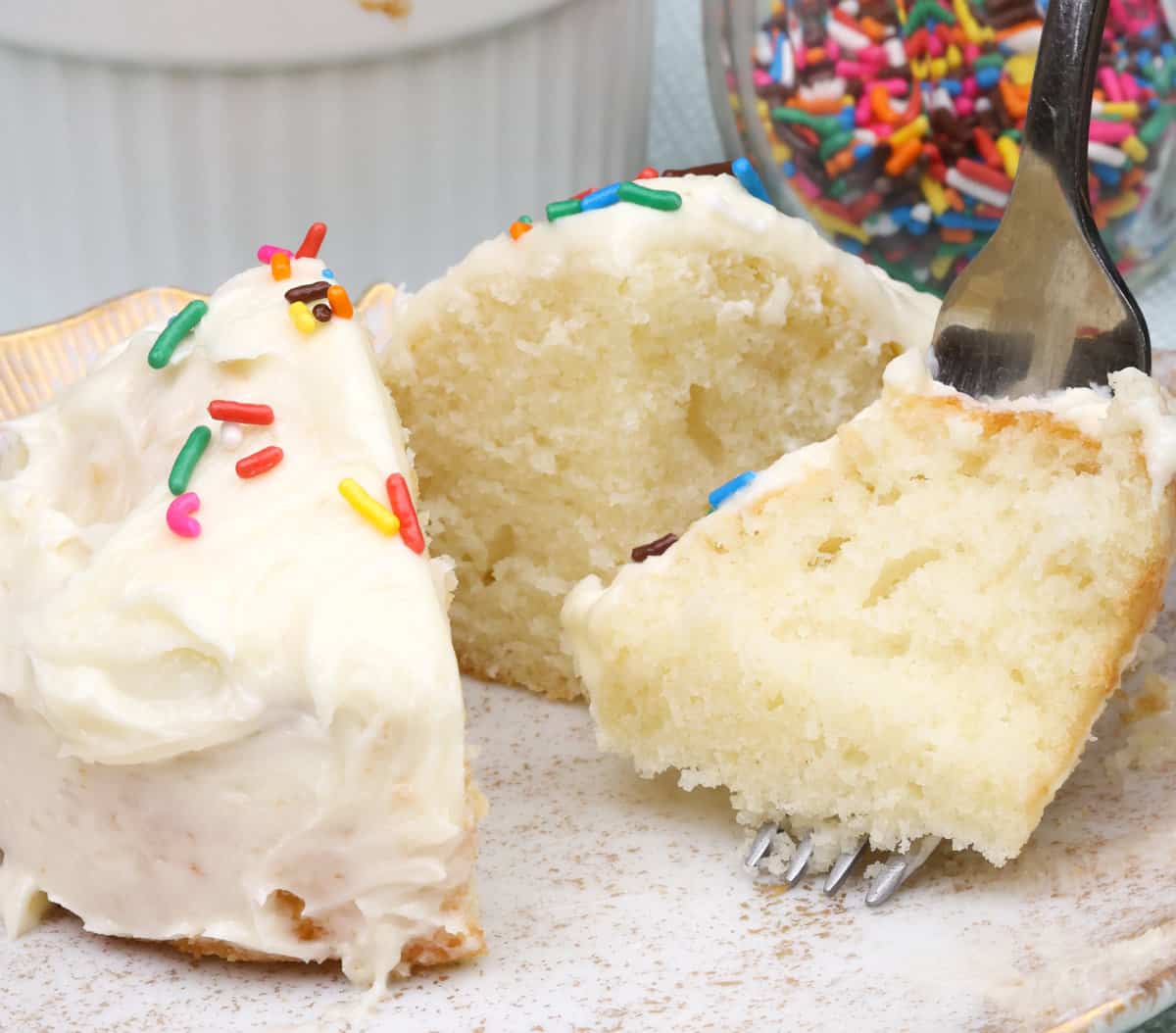 a slice of white cake with the fork on the side and a jar of sprinkles in the background