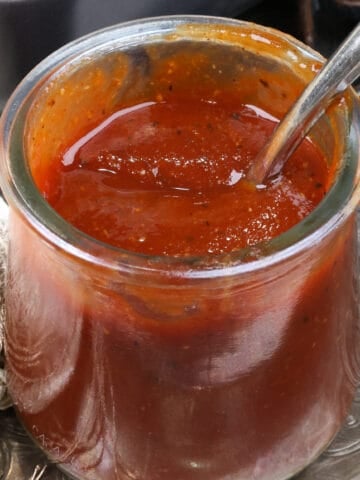 a small jar of homemade bbq sauce on a silver tray next to a beige napkin