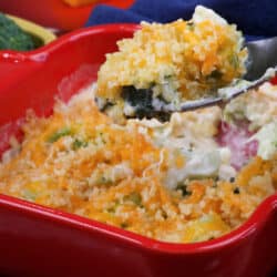 broccoli casserole topped with melted cheddar cheese in a red baking dish with a fork on the side