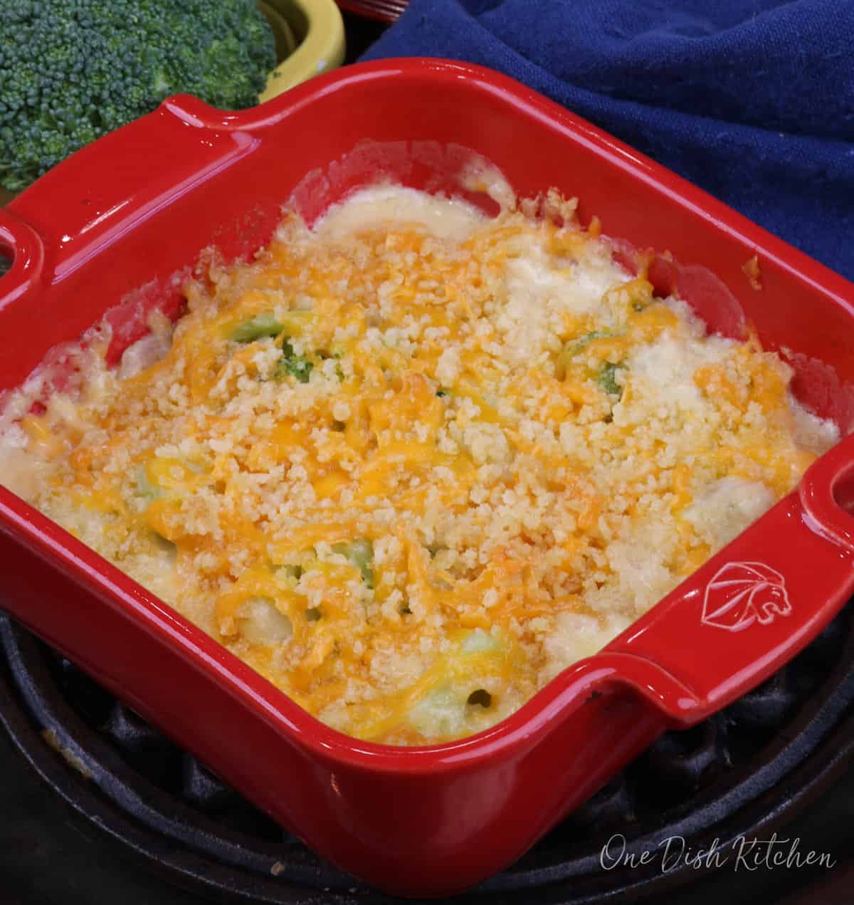 a mini broccoli cheese casserole in a red baking dish next to a head of fresh broccoli.