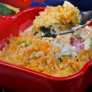 broccoli casserole topped with melted cheddar cheese in a red baking dish with a fork on the side.