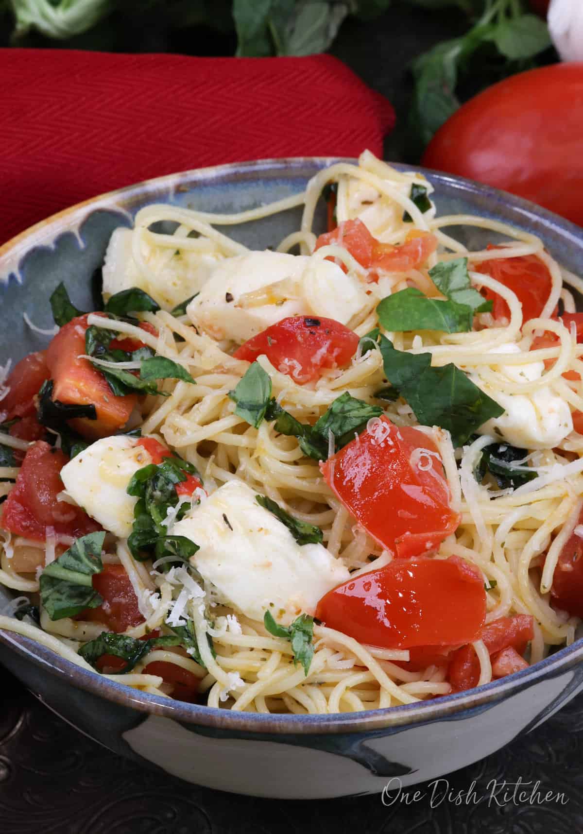 a bowl of caprese pasta next to a red napkin and fresh basil.