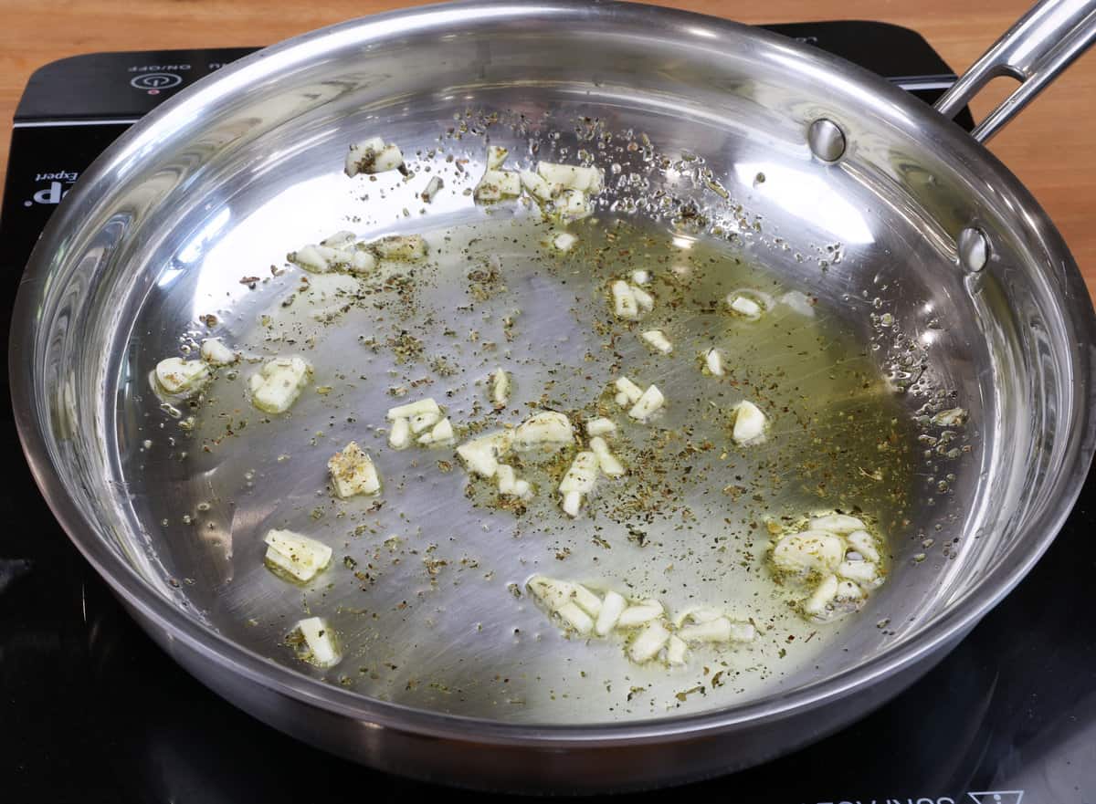garlic cooking with Italian seasoning and olive oil in a skillet.