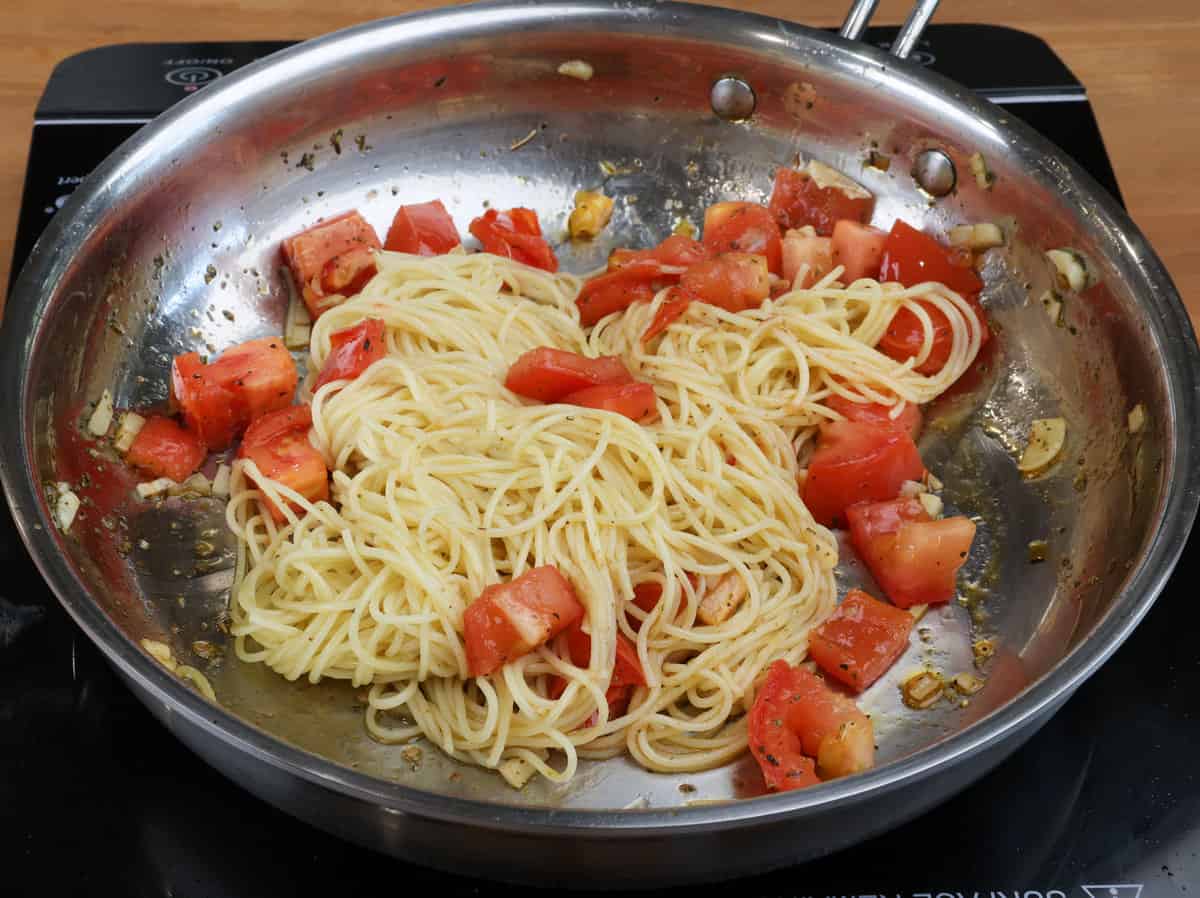 cooked spaghetti mixed with tomatoes and garlic in a skillet.