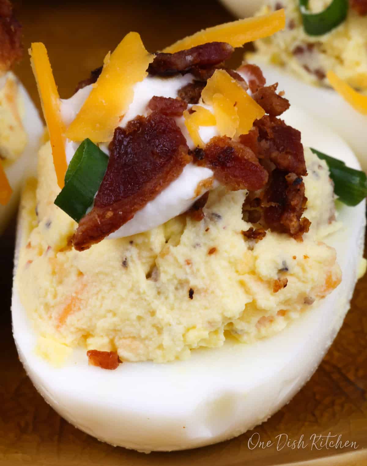 one deviled egg topped with bacon, cheese, and sour cream
