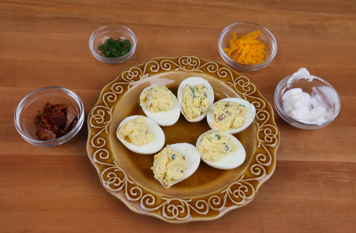 6 deviled eggs on a plate next to four bowls of garnishes.