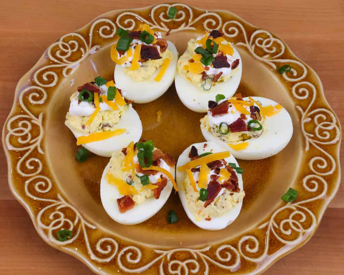 a plate of deviled eggs with bacon topped with chopped green onions.