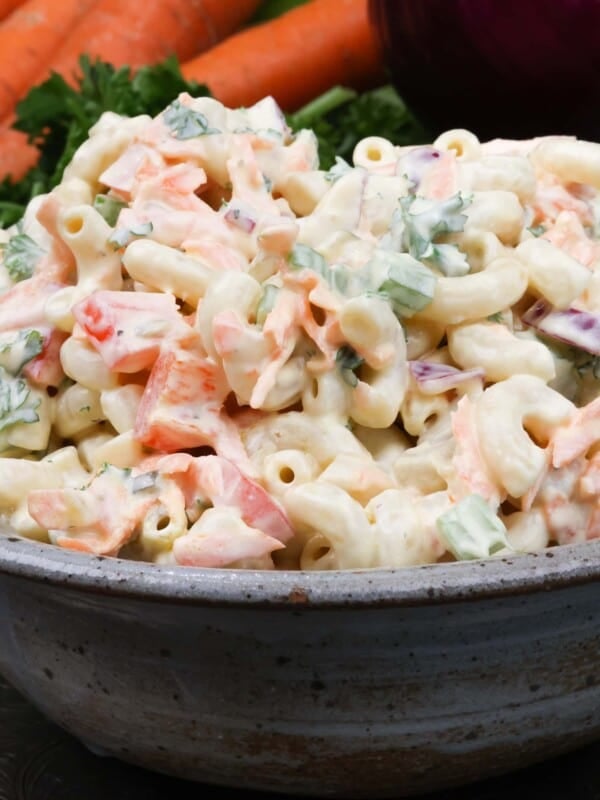 a small bowl of macaroni salad on a silver tray next to a red onion and four carrots