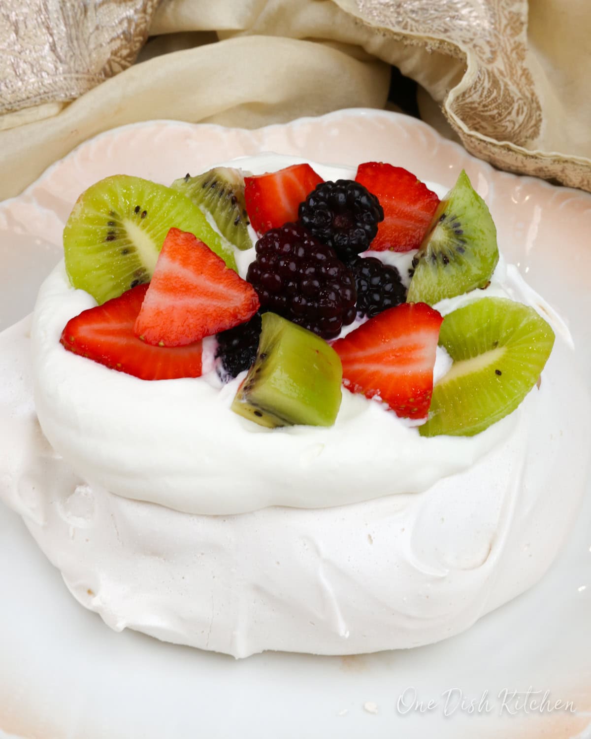 a mini pavlova on a white plate topped with fresh fruit.