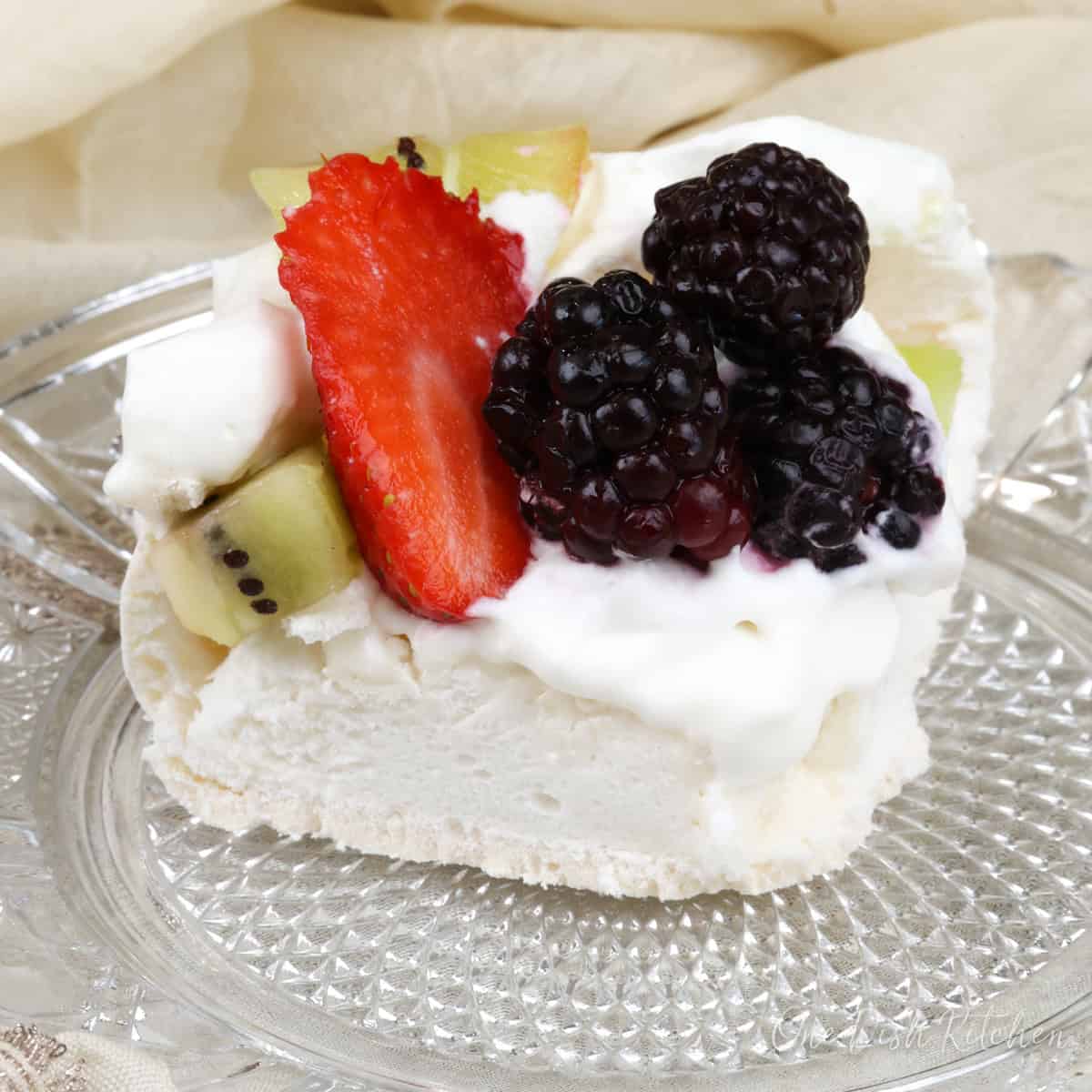 a mini pavlova topped with fresh fruit on a white plate next to a cream napkin.