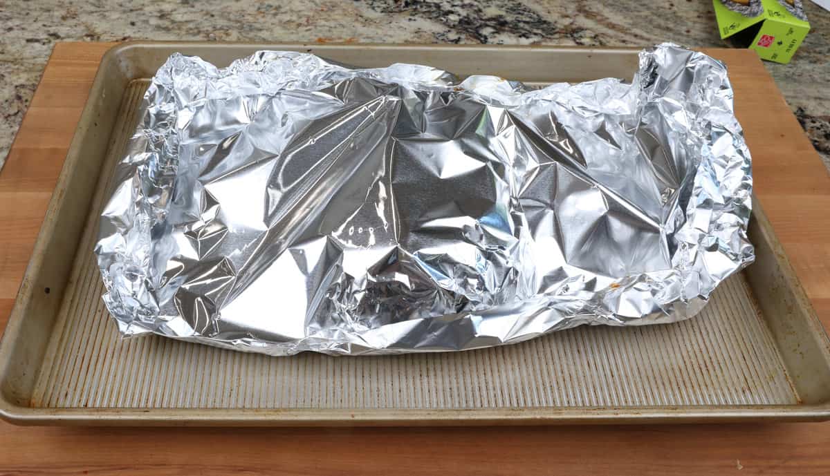 a half rack of ribs in a foil sealed pouch on a baking sheet