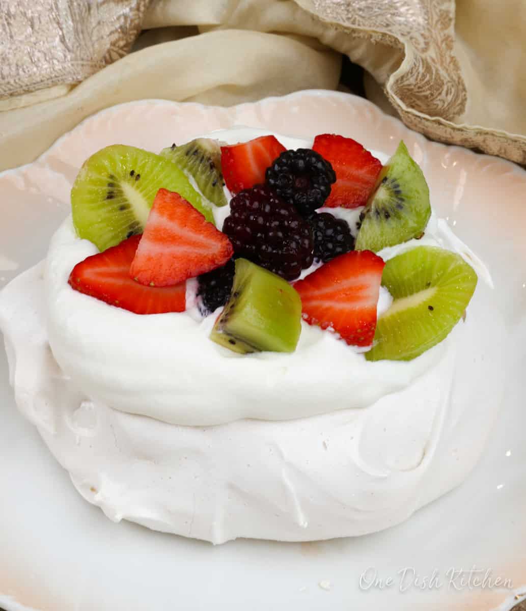 a mini pavlova topped with whipped cream and fresh fruit.
