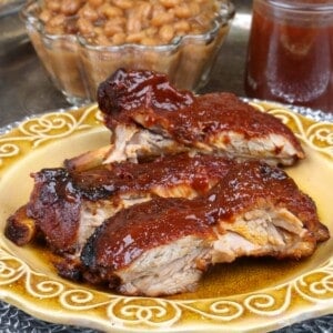 baby back ribs on a plate next to a jar of bbq sauce and a bowl of beans