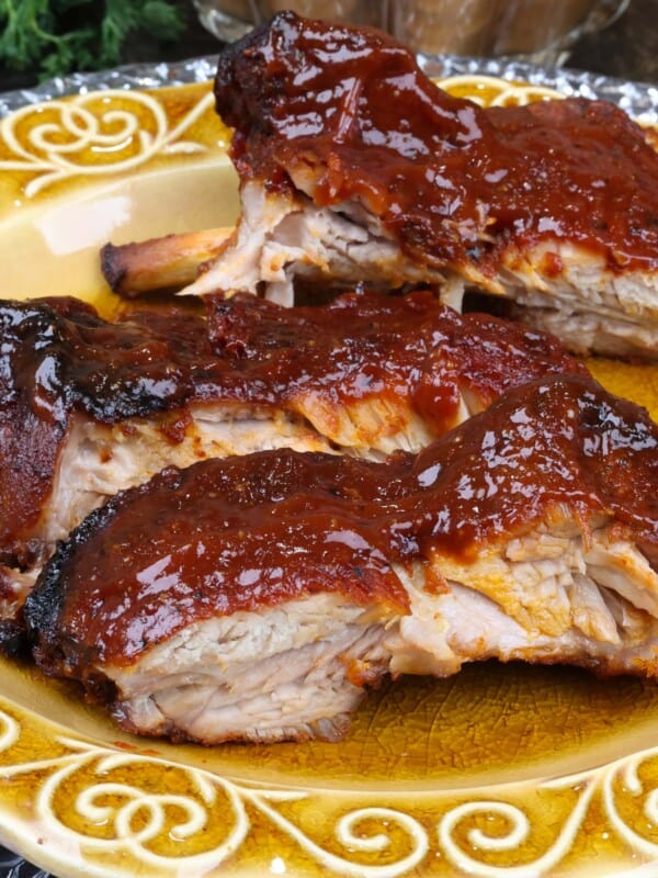 three baby back ribs with BBQ sauce on a gold plate next to a bowl of baked beans