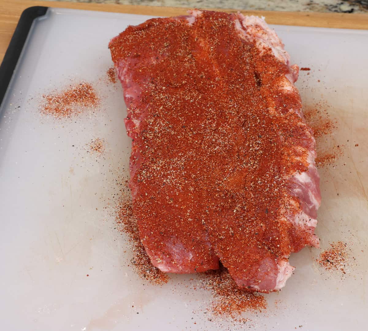 a half rack of ribs on a cutting board coated with dry rub seasoning.