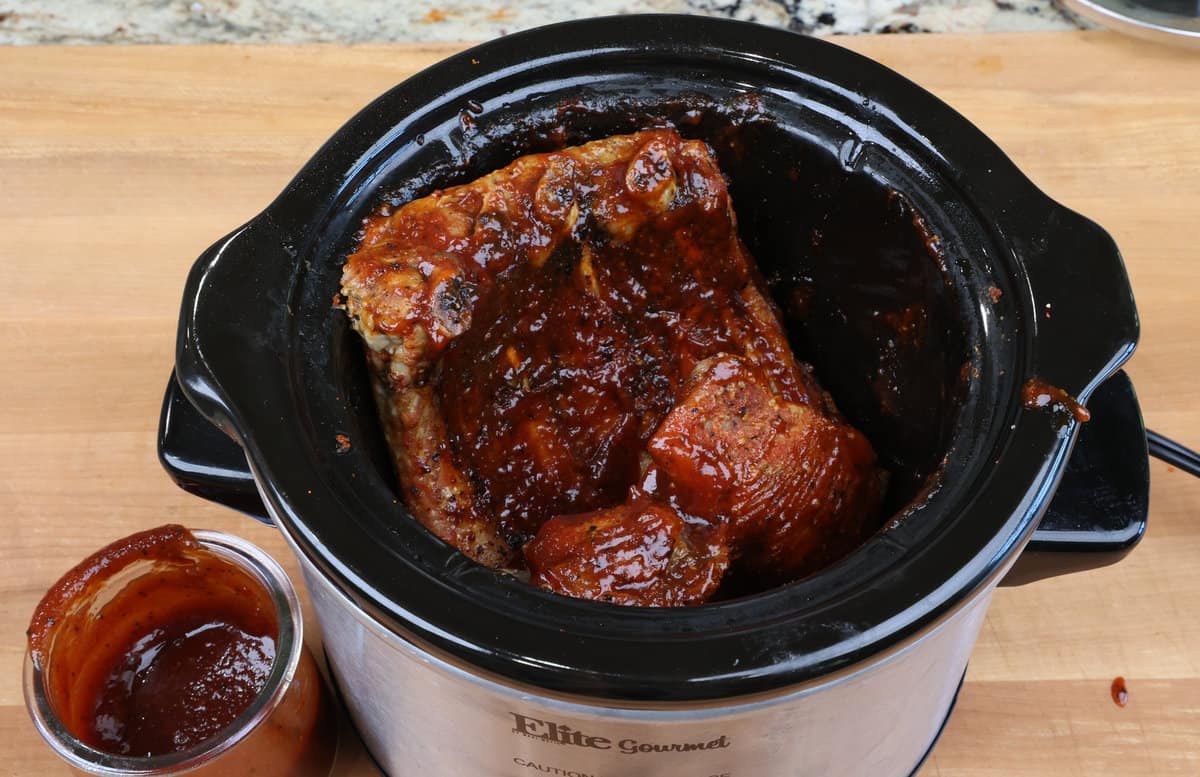 adding bbq sauce to baby back ribs in a slow cooker.