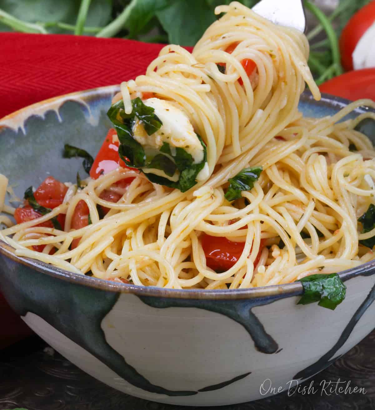 a single serving of caprese pasta with fresh mozzarella and basil on a fork.