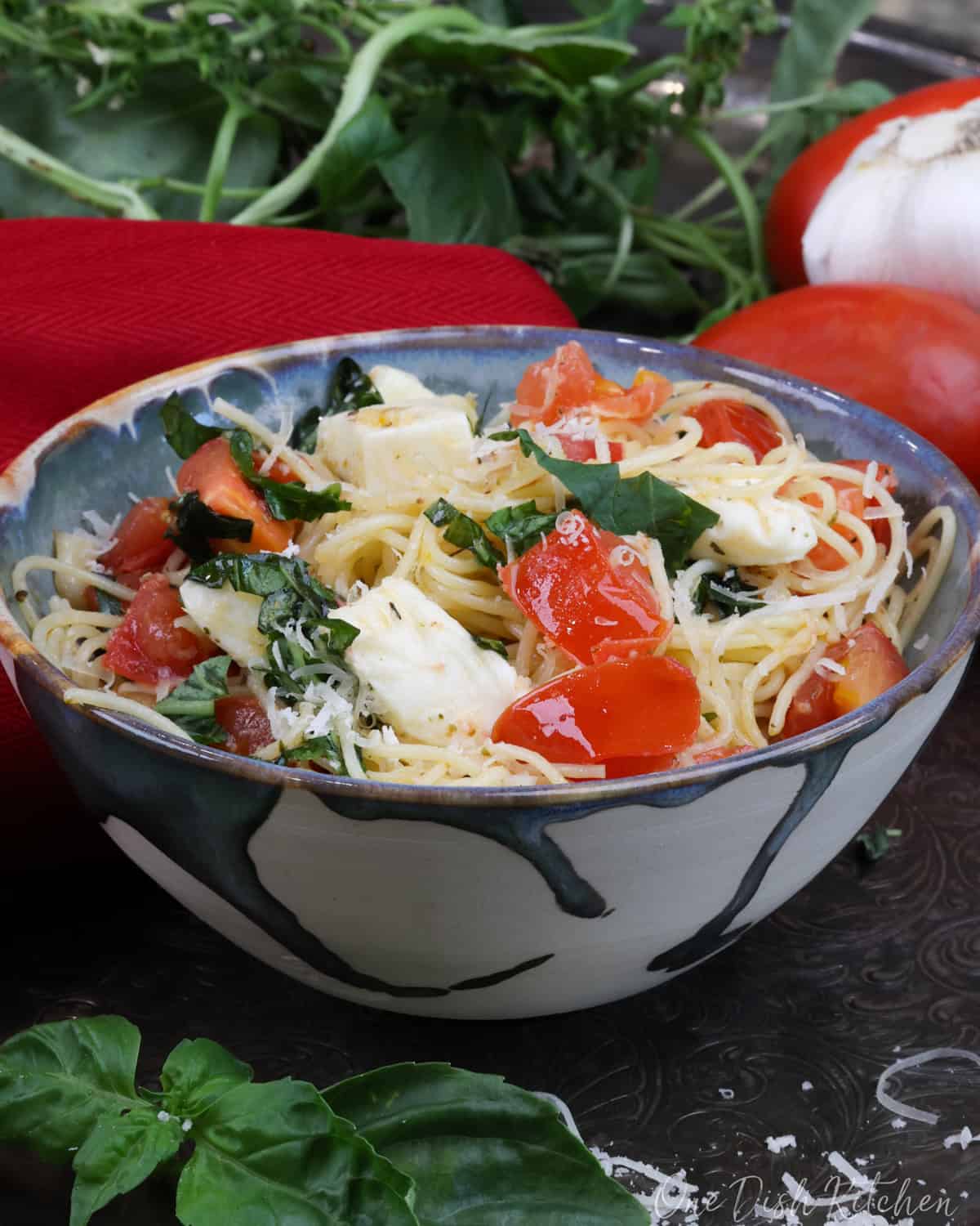 a bowl of angel hair pasta mixed with mozzarella cheese, fresh chopped tomatoes, and fresh torn basil.