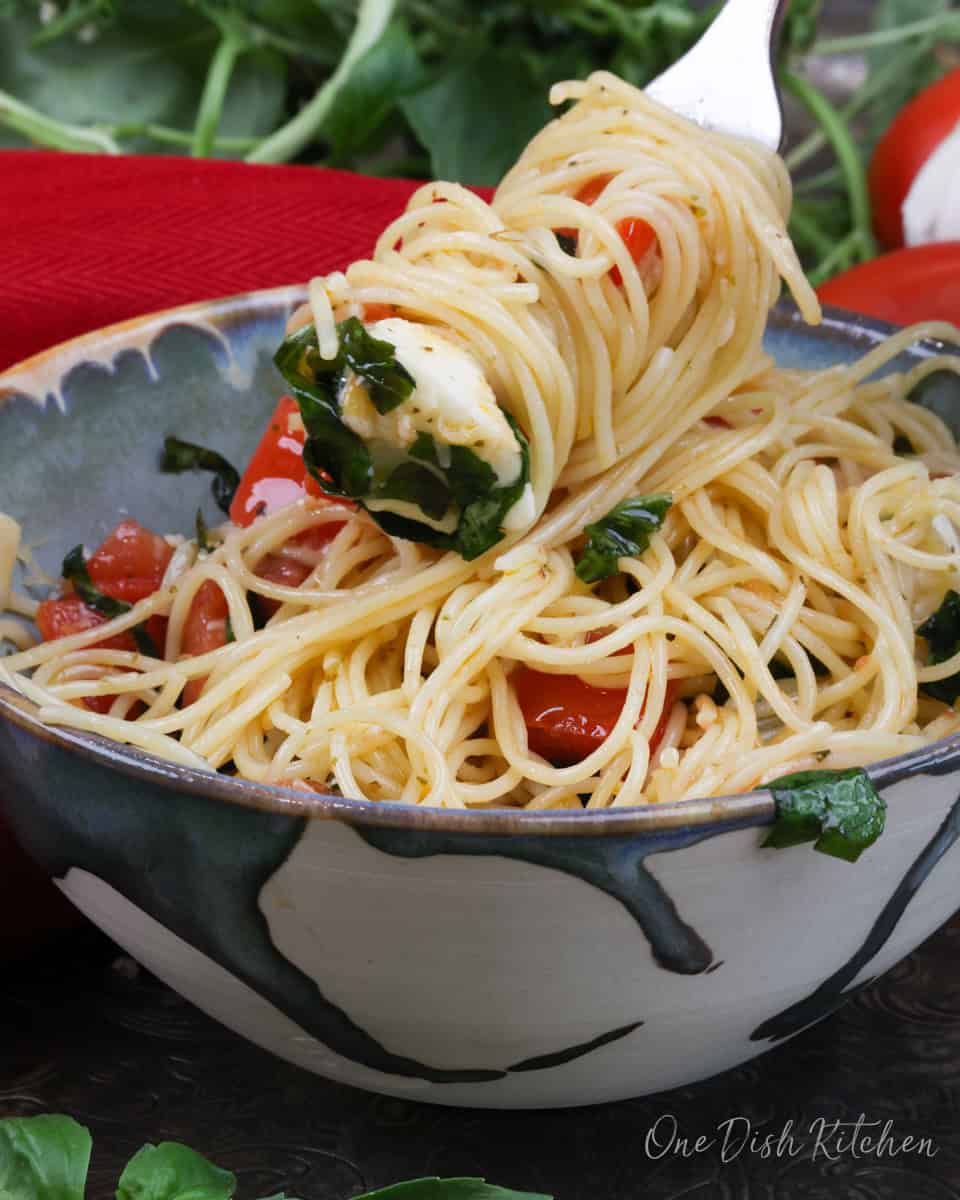 a fork filled with caprese pasta over the bowl.