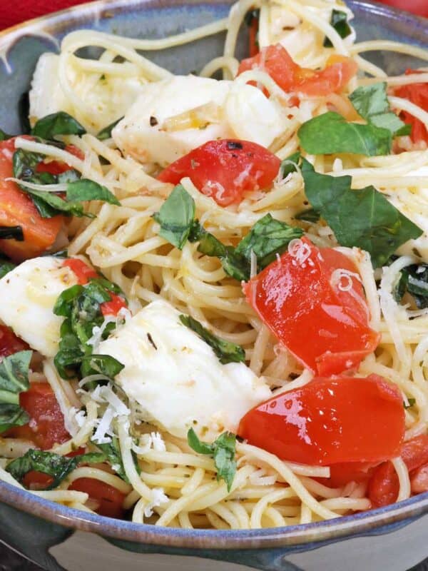 a bowl of angel hair pasta mixed with mozzarella cheese, fresh chopped tomatoes, and fresh torn basil.
