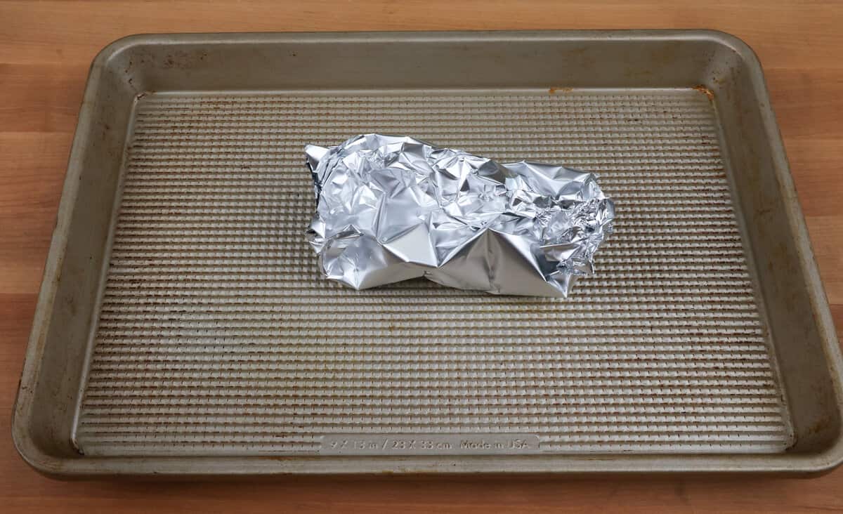 a head of garlic wrapped in aluminum foil on a baking sheet.