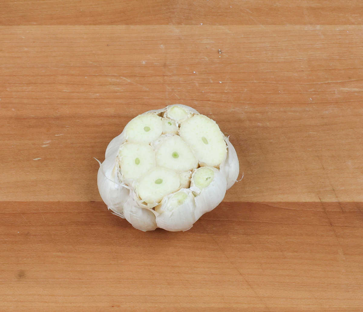 a head of garlic with the top cut off on a wooden cutting board.