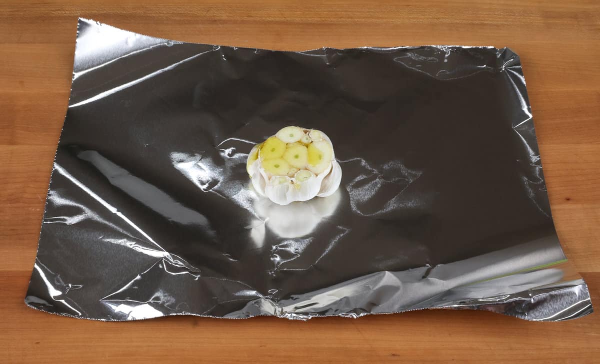 a head of garlic with olive oil drizzled on top on a sheet of aluminum foil.