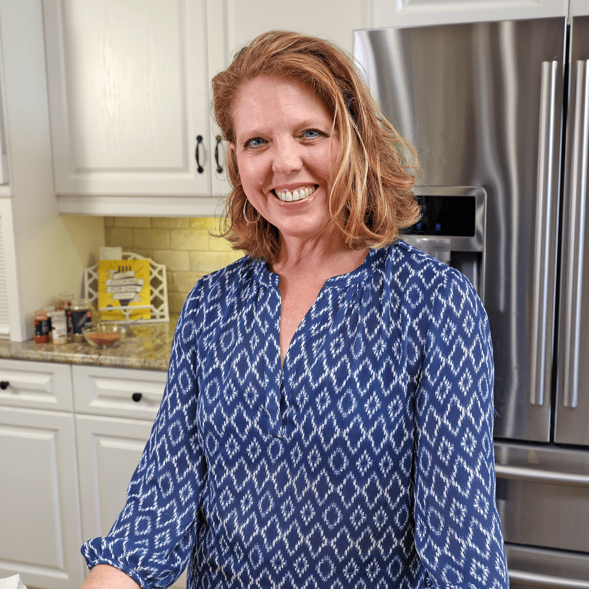 Joanie standing in kitchen with blue shirt that has a white diamond pattern