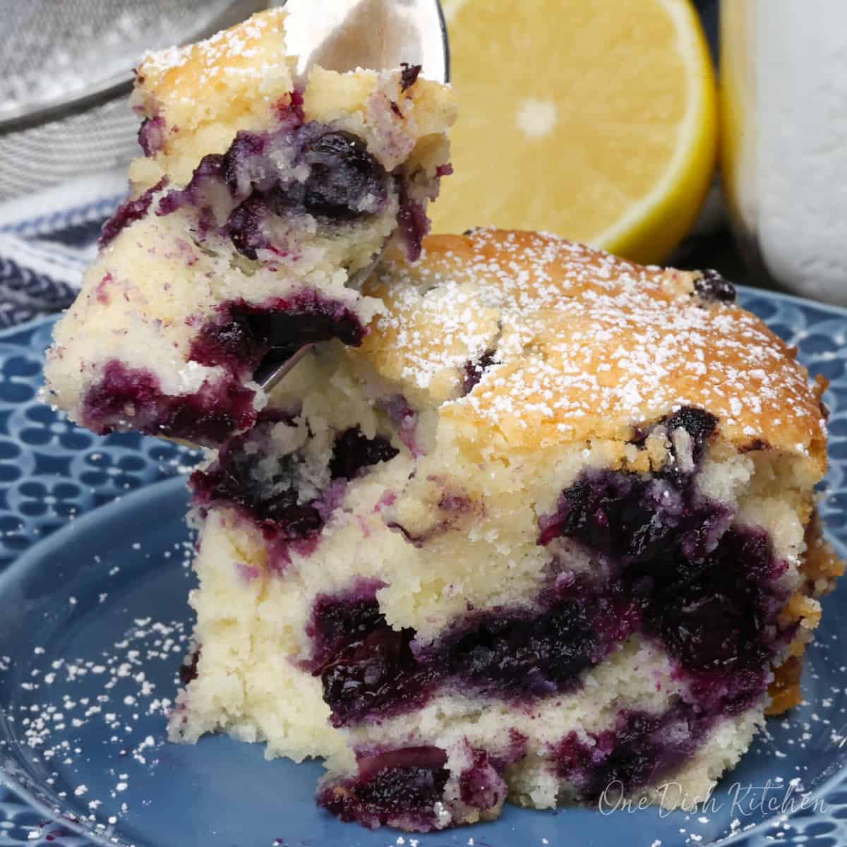 blueberry cake on a small plate with a fork on the side.