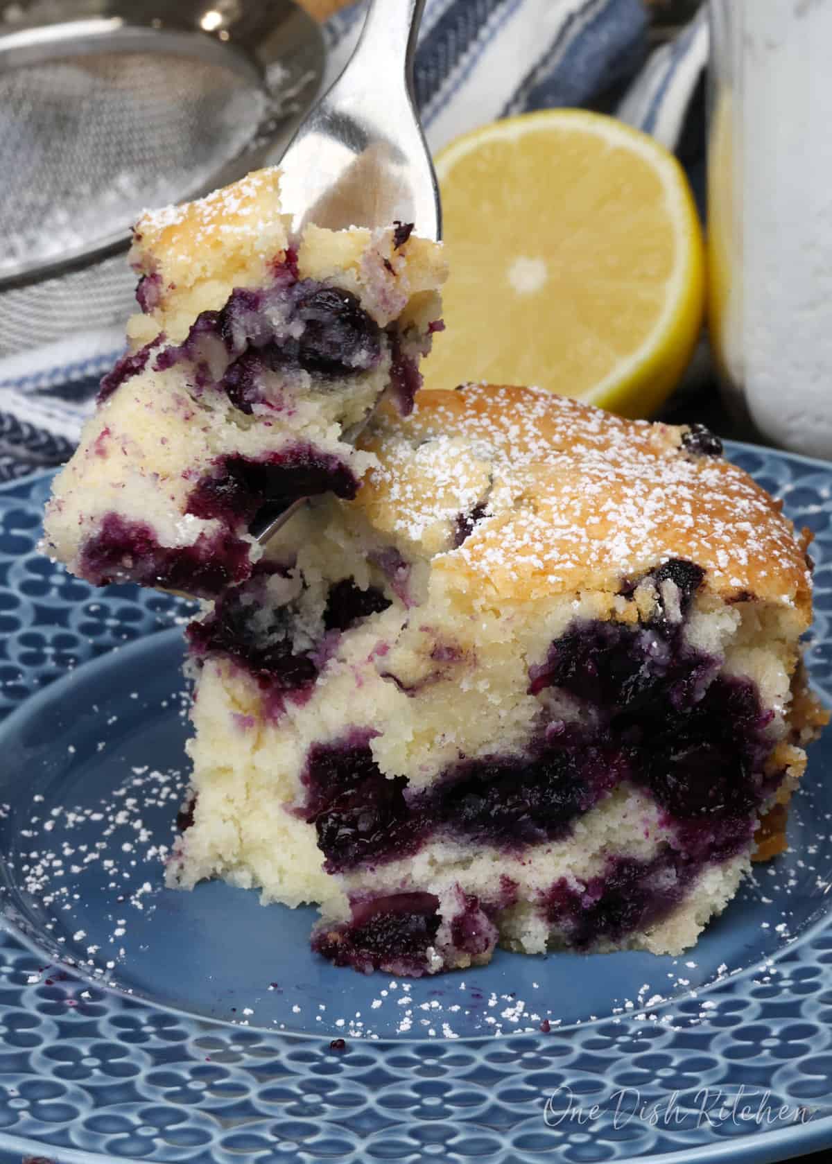 blueberry cake on a fork next to a larger slice.