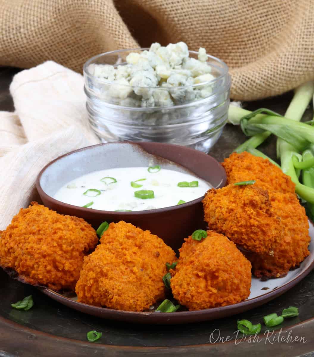 5 buffalo cauliflower nuggets on a plate next to a bowl of blue cheese dressing.