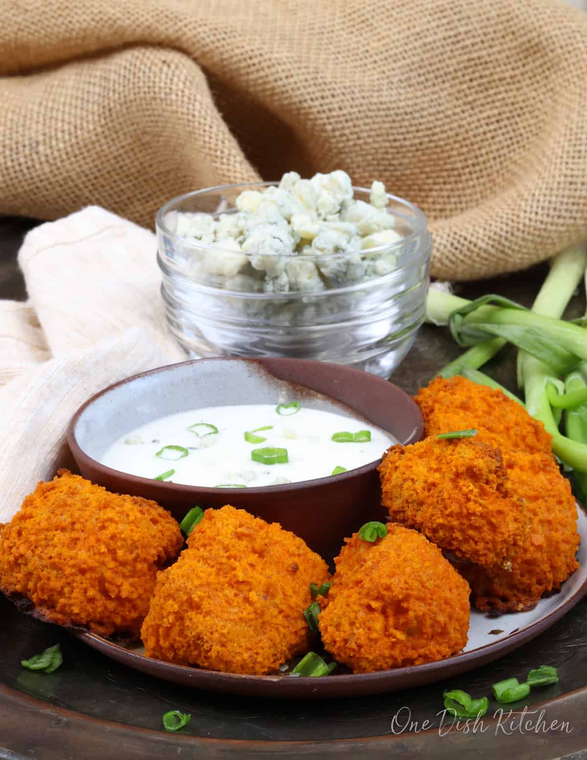 5 buffalo cauliflower nuggets on a plate next to a bowl of blue cheese dressing.