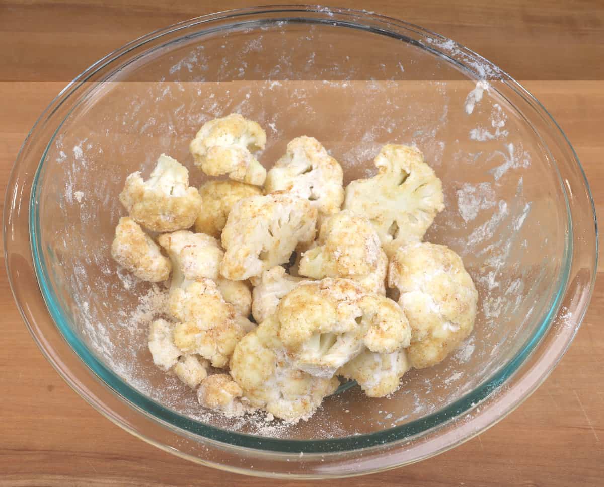 cauliflower florets in a bowl tossed with oil, flour, and spices.