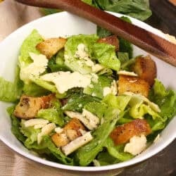 a small caesar salad in a bowl with a wooden spoon on the side.