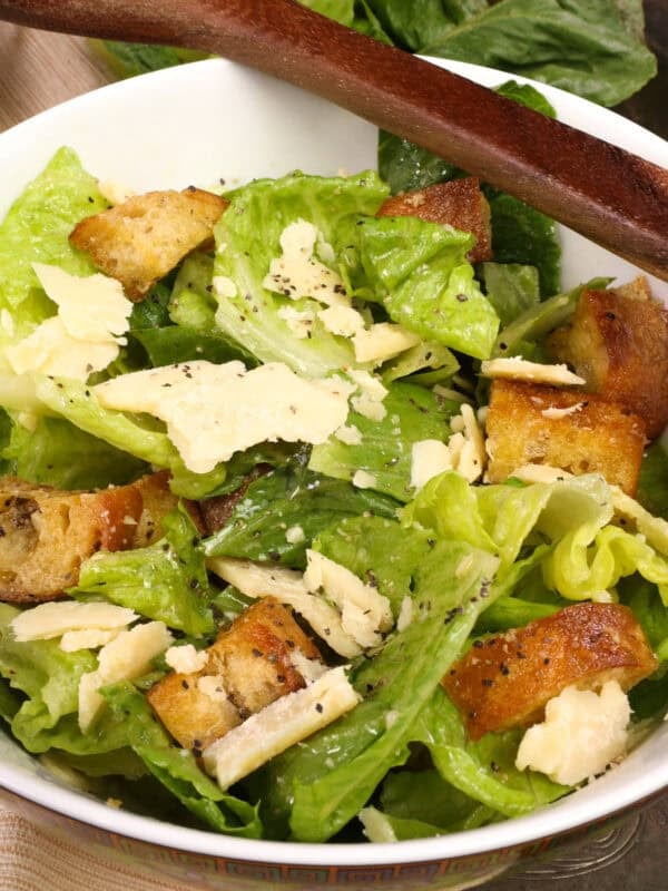 a small caesar salad in a bowl with a wooden spoon on the side.