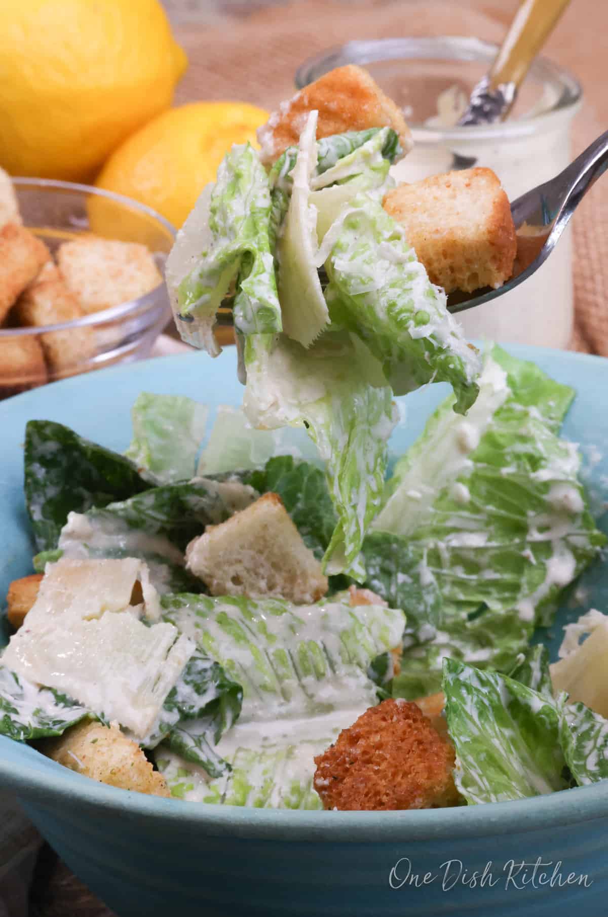 a fork filled with caesar salad and a crouton above a big bowl of salad.