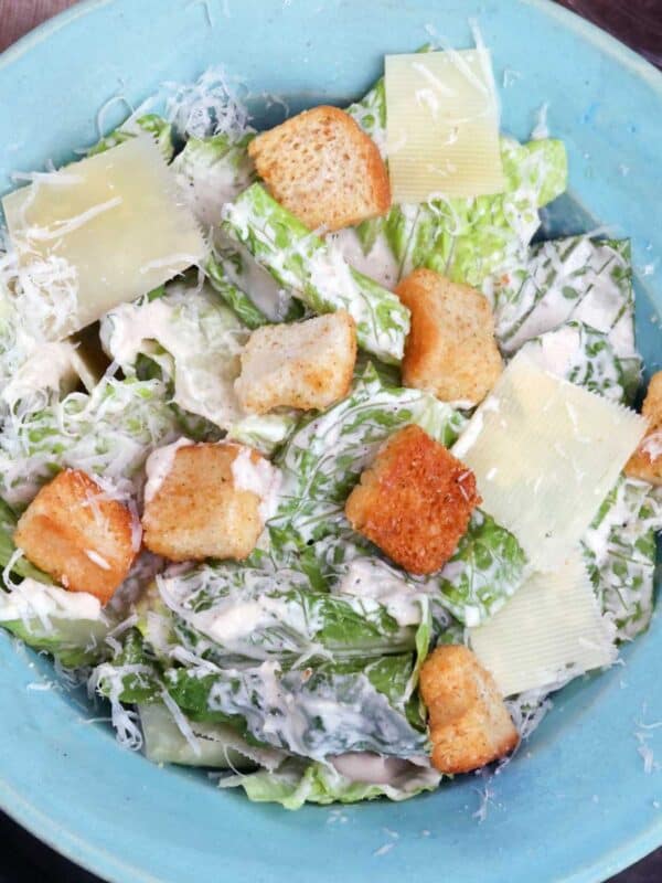 a blue bowl filled with caesar salad topped with parmesan cheese and croutons.