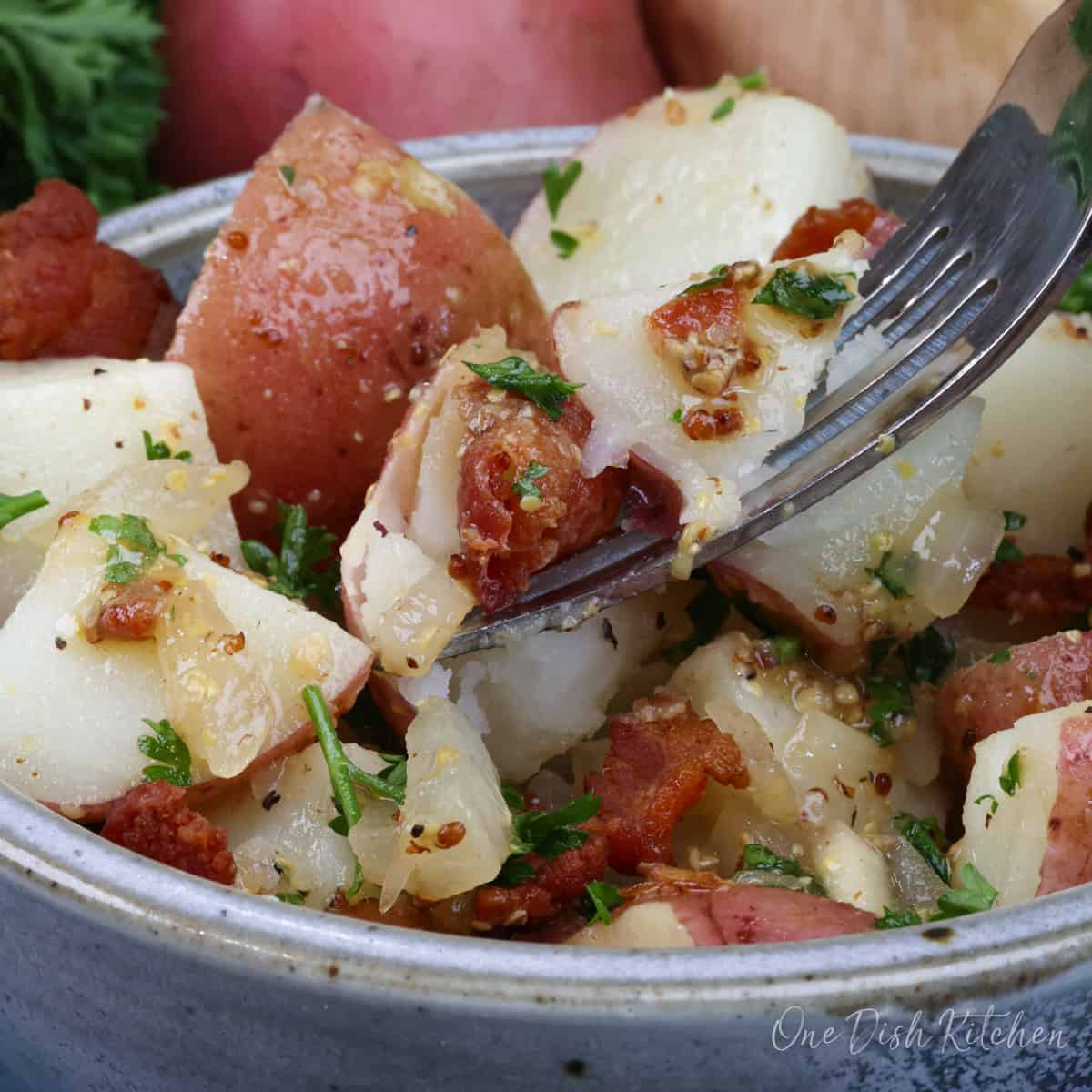 a single serving of warm german potato salad in a bowl with a fork raised above the bowl.