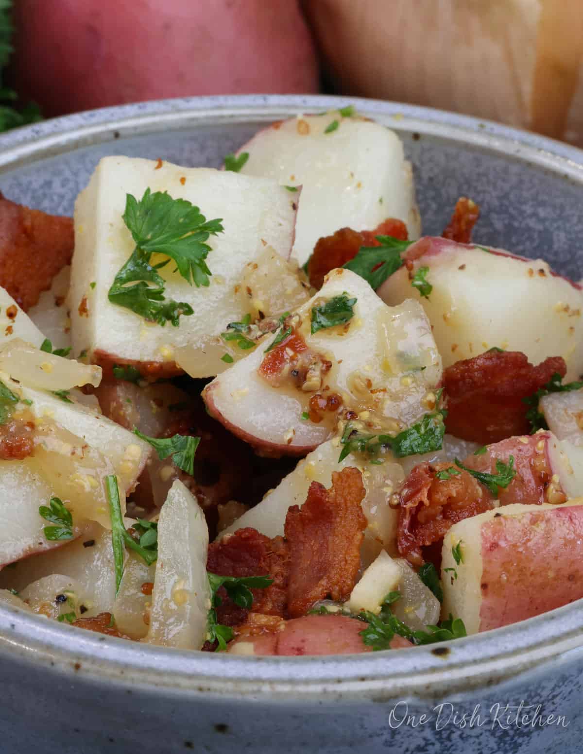 german potato salad in a bowl topped with stone ground mustard and chunks of bacon and parsley.