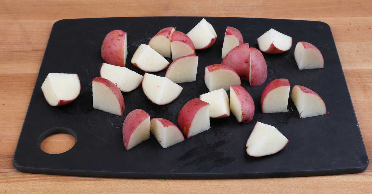 small red potatoes cut into bite sized pieces on a cutting board.