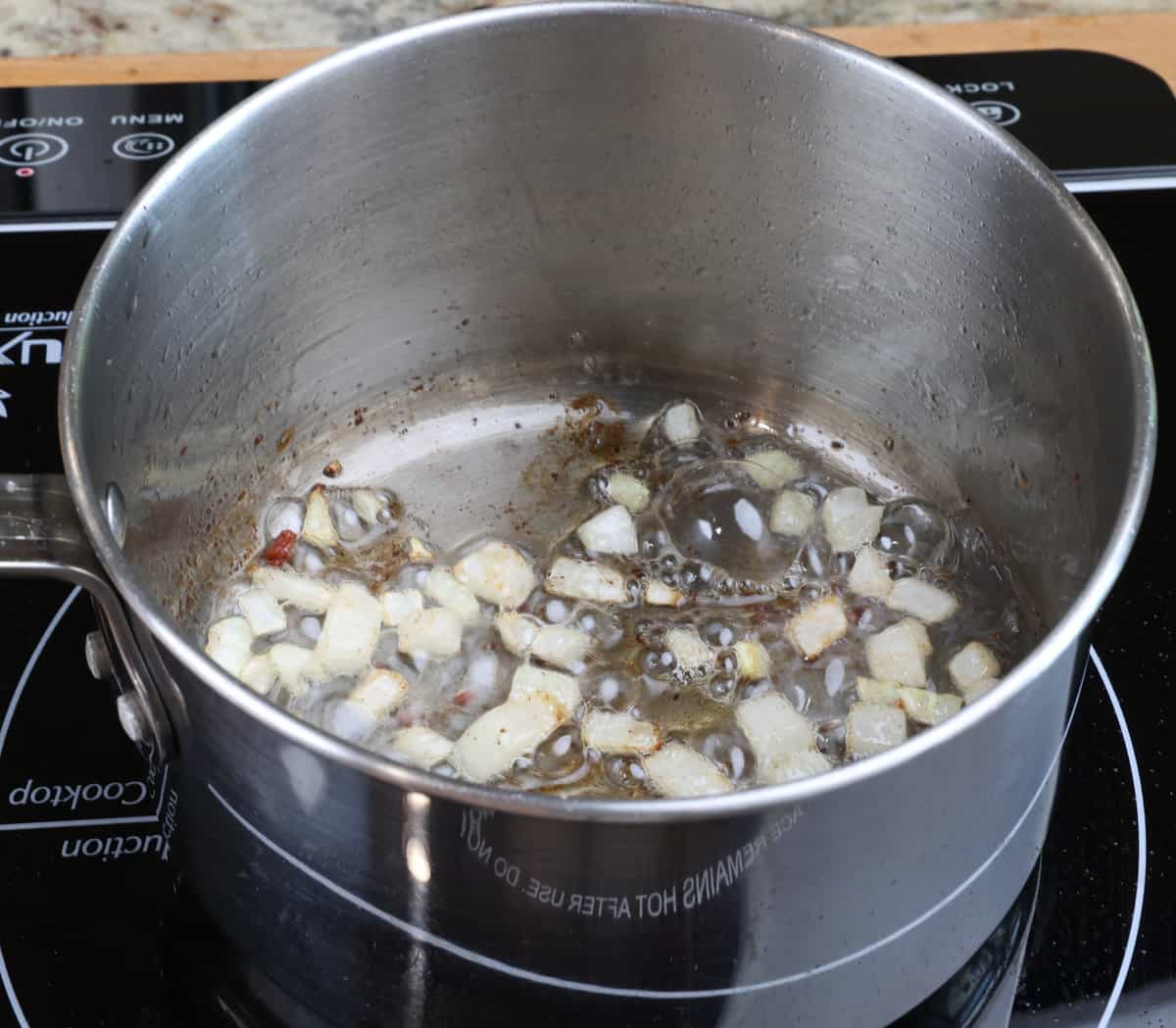 chopped onions cooking in bacon drippings in a small pot on the stove.