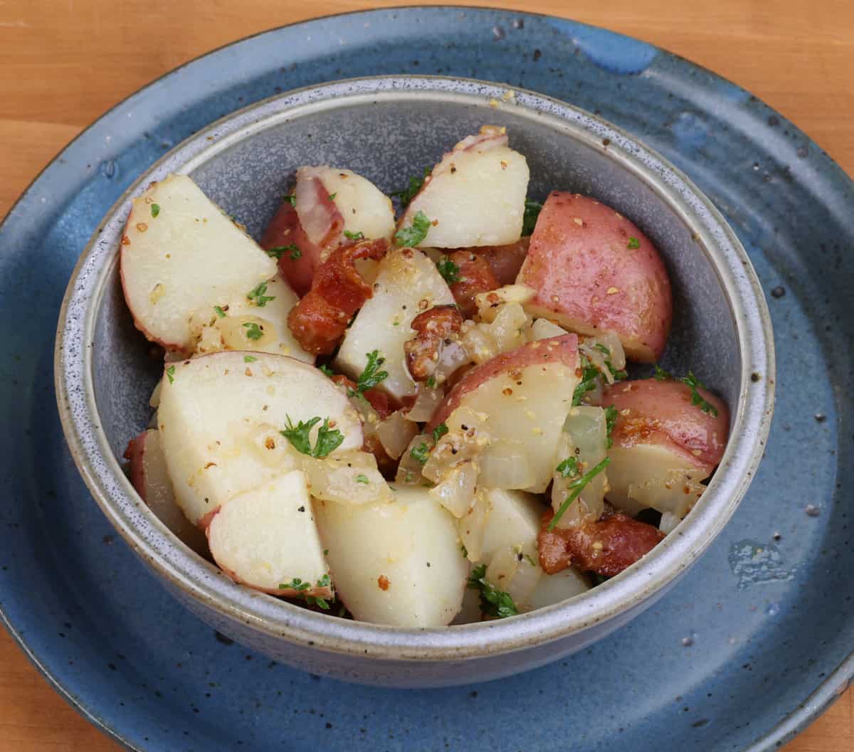 a bowl of warm potato salad on a wooden table.